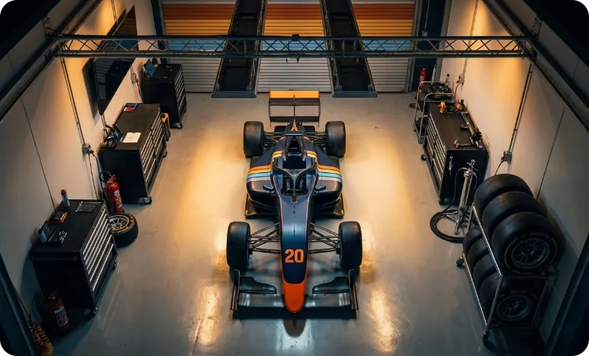 #20 car at rest in garage bay — overhead view, four-stripe livery, tire stacks, amber workshop light