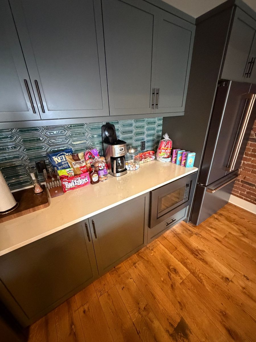 A kitchen counter staged with snacks, a coffee maker, a jar of candy and boxes, next to the refrigerator