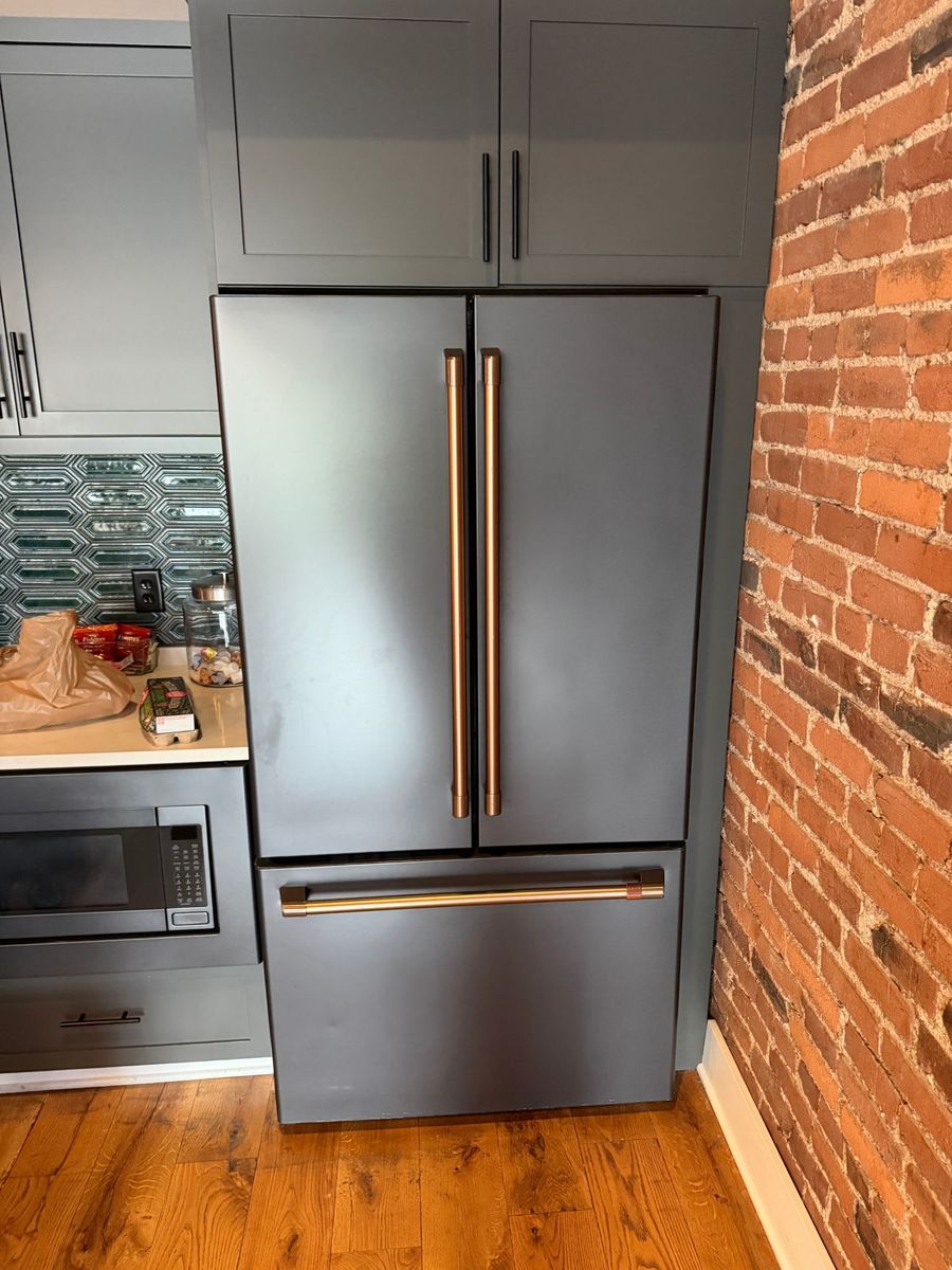 A closed French-door refrigerator with copper handles, beside a brick wall